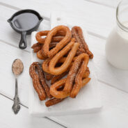 Homemade churros with chocolate on a white wooden background.