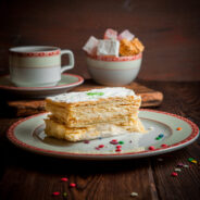 Side vew puff cake with cup of tea and sugar in round plate on wood background