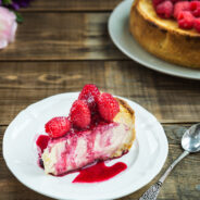 Slice of Homemade Vanilla Cheesecake with Raspberries and Berry Sauce on Dark Rustic Background